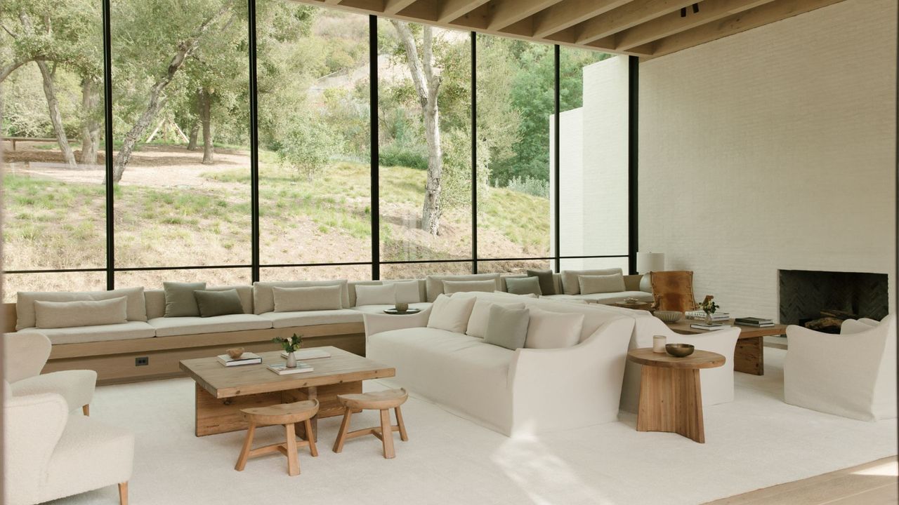 White and wood scheme living room with multiple seating areas, back to back couches, low slung stools, coffee tables, large windows with view outside, beams