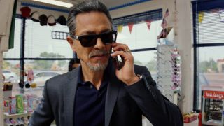 Benjamin Bratt takes a phone call while sharply dressed in Poker Face.