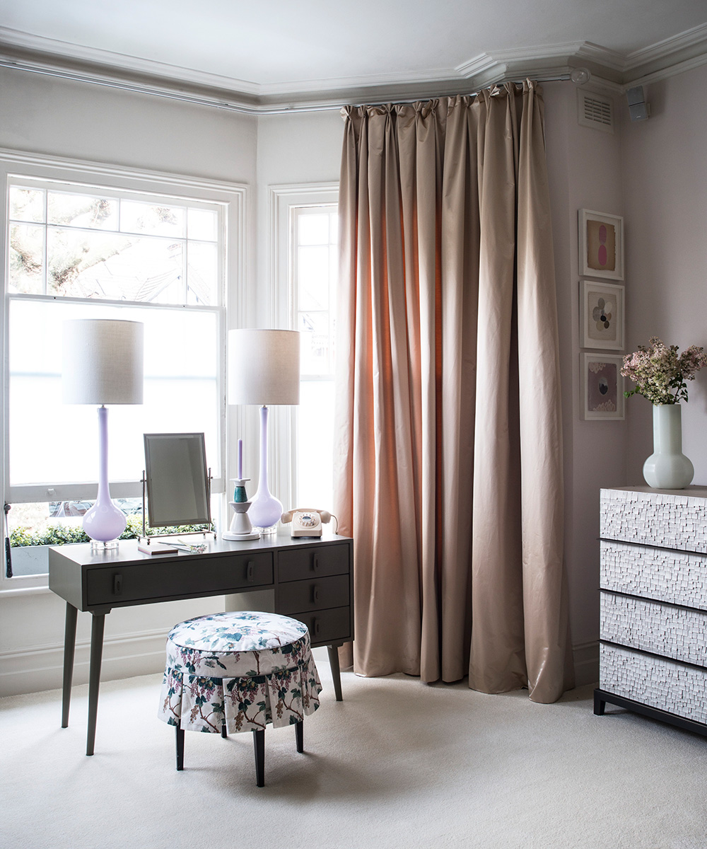 A dressing table in front of a large window with pink drapes