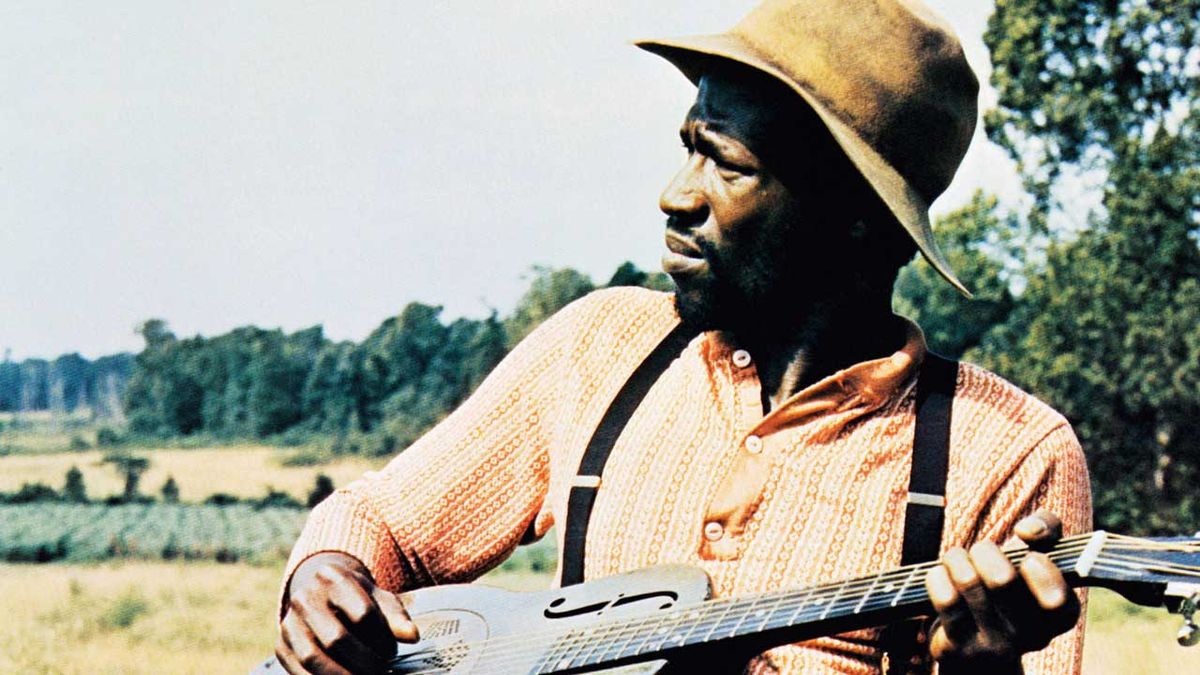 Taj Mahal playing an acoustic guitar in a field