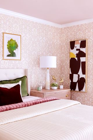 A pink themed bedroom with a patterned wallpaper, a pink ceiling, and a styled bed with velvet cushions
