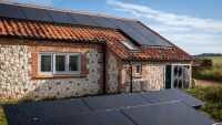 Solar panels on the roof of a cottage and a heat pump outside of a stone wall of the house
