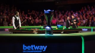 UK Championship trophy in front of two players playing snooker