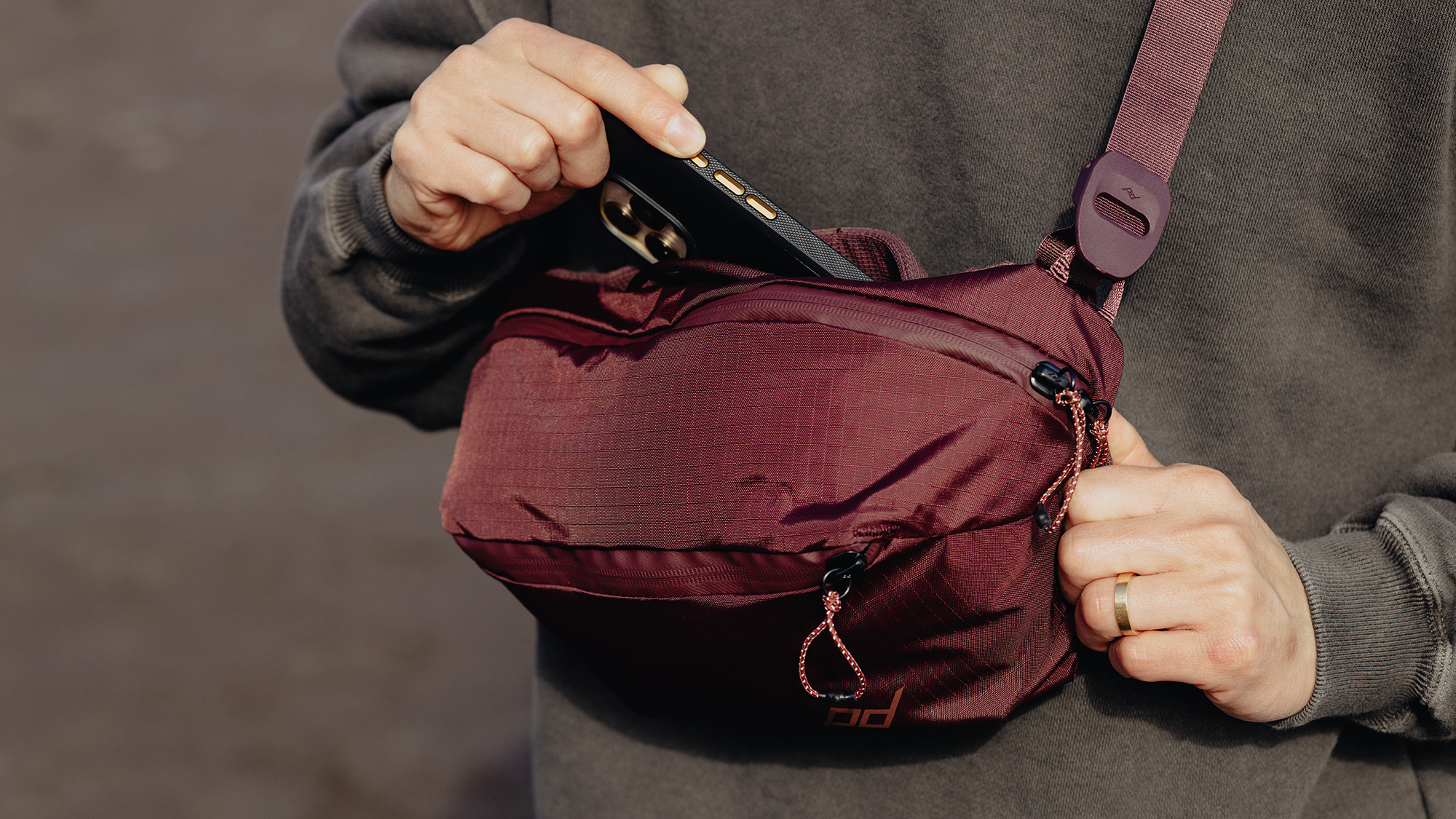 Peak Design Outdoor Sling 4L lifestyle image of person pulling phone from Sling 4L