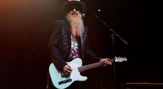 Billy Gibbons of ZZ Top smiles as he plays his Daphne Blue Fender Esquire onstage. He wears a wide brimmed hat, sunglasses, and has his trademark beard.