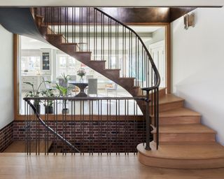 Wide timber and metal staircase, looking out through glass windows to dining room, exposed brickwork and metal detailing.