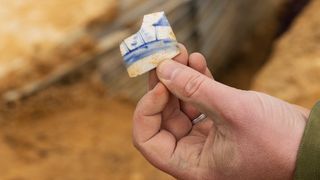 A person holds a white-and-blue ceramic shard.