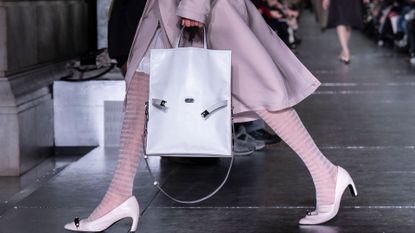 A model walks at Tory Burch with a white buckled tote bag