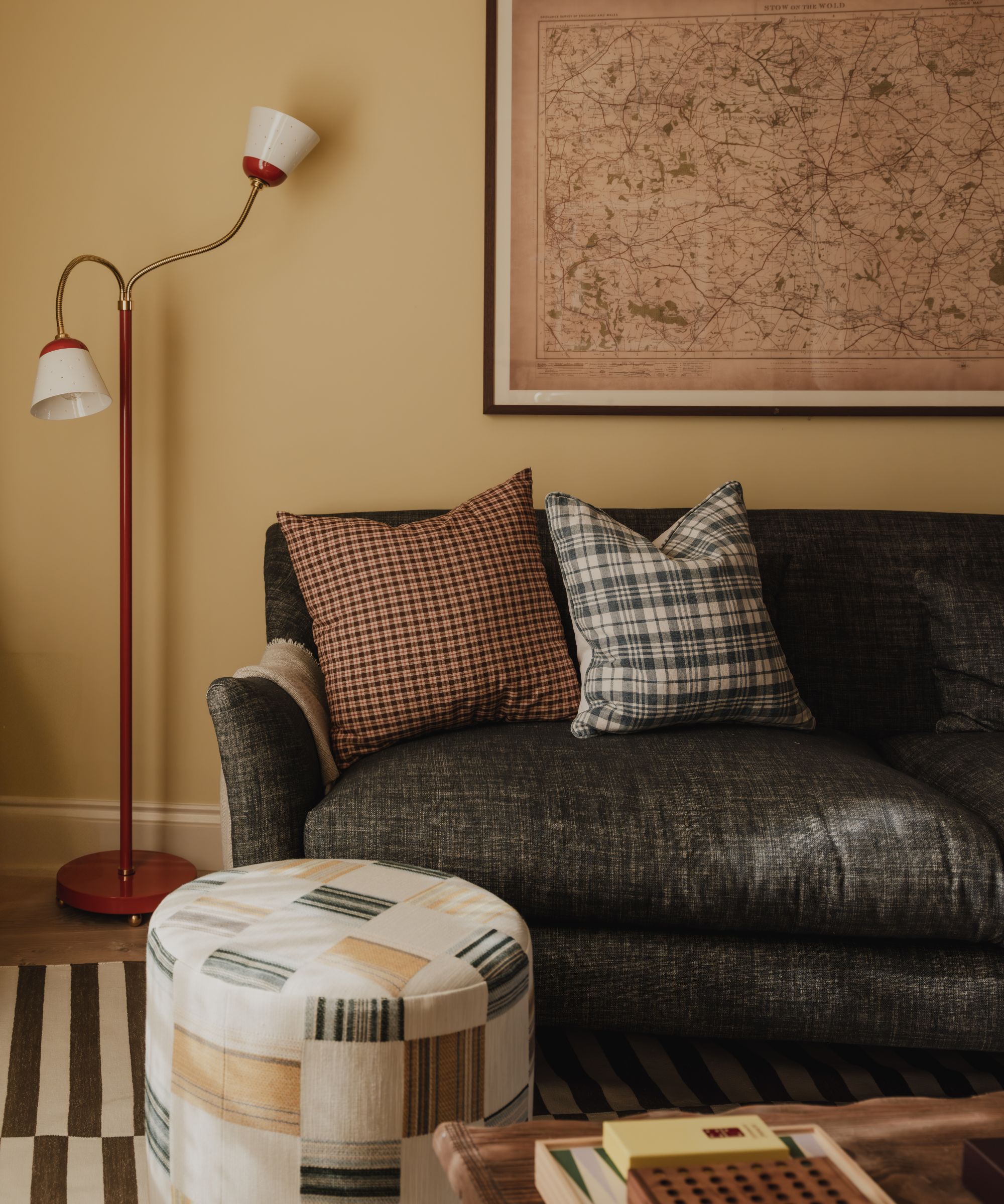 a yellow painted living room with charcoal sofa, a map of the cotswolds, patchwork pouffe and floor lamp from Original BTC