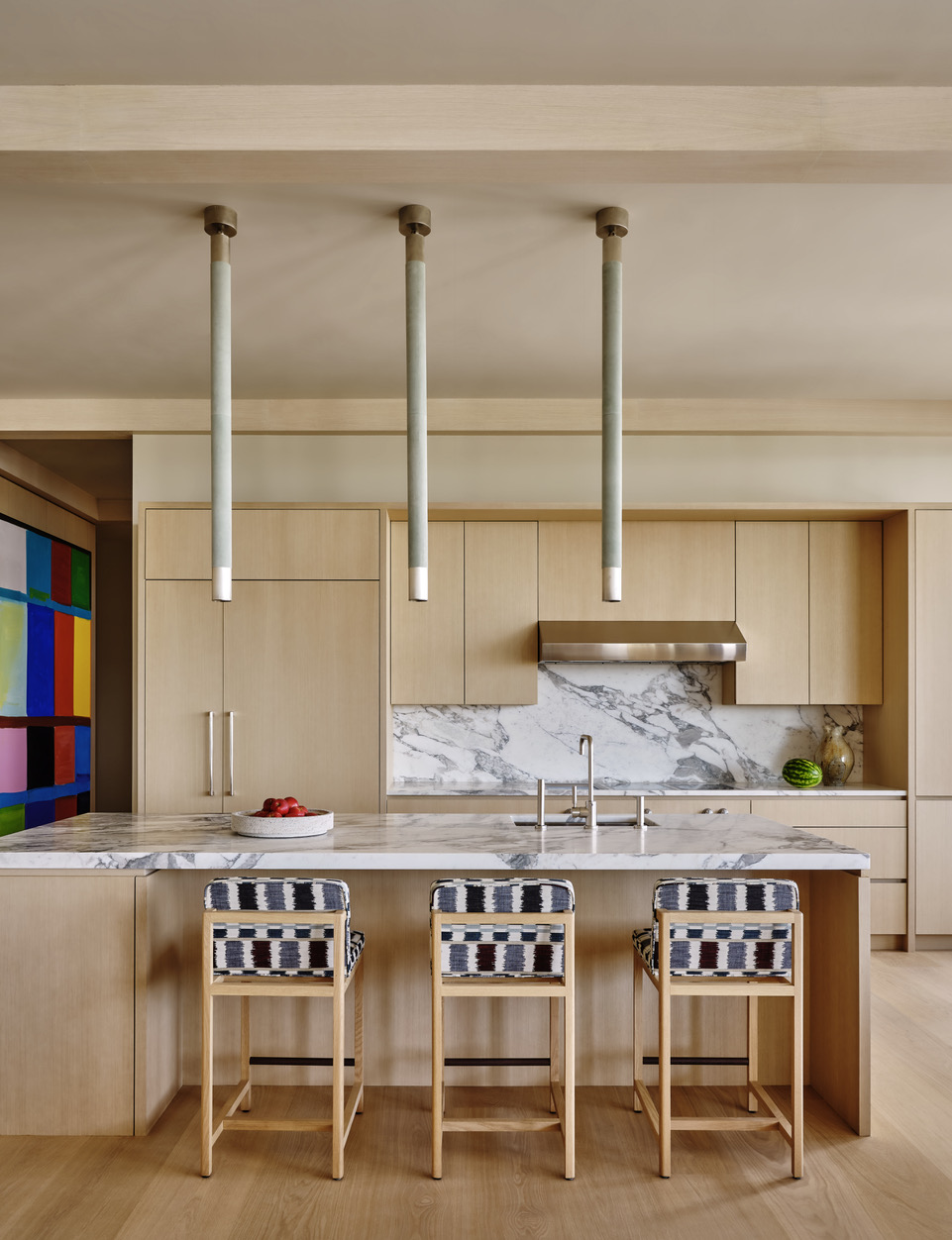 A wooden kitchen with a marble backsplash, and island, and above that, three long pendants
