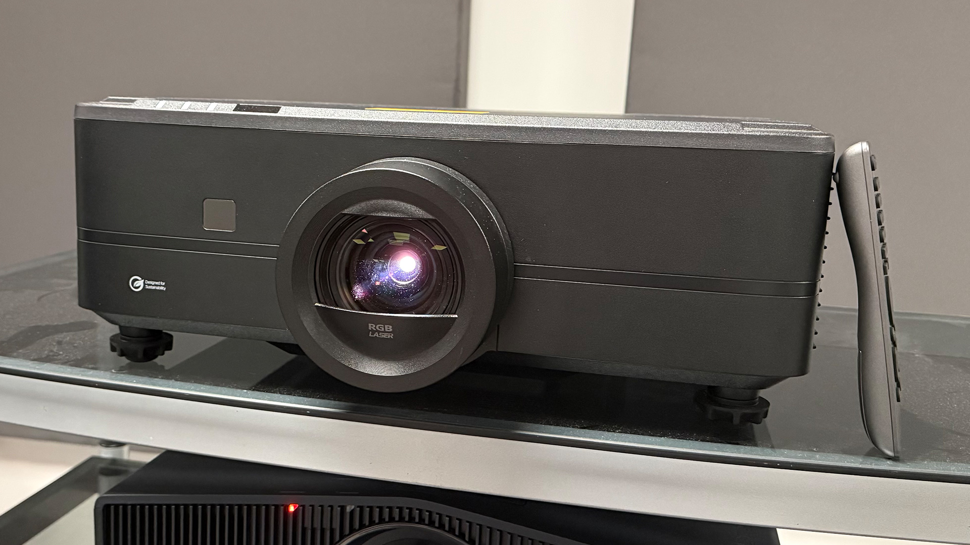 Optoma UHZ78LV home cinema projector on glass topped unit with remote leaning up against it