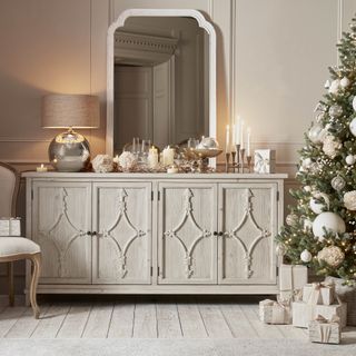 A cream sideboard with a selection of candles and metallic lamps amps on top of it as well as a large statement mirror