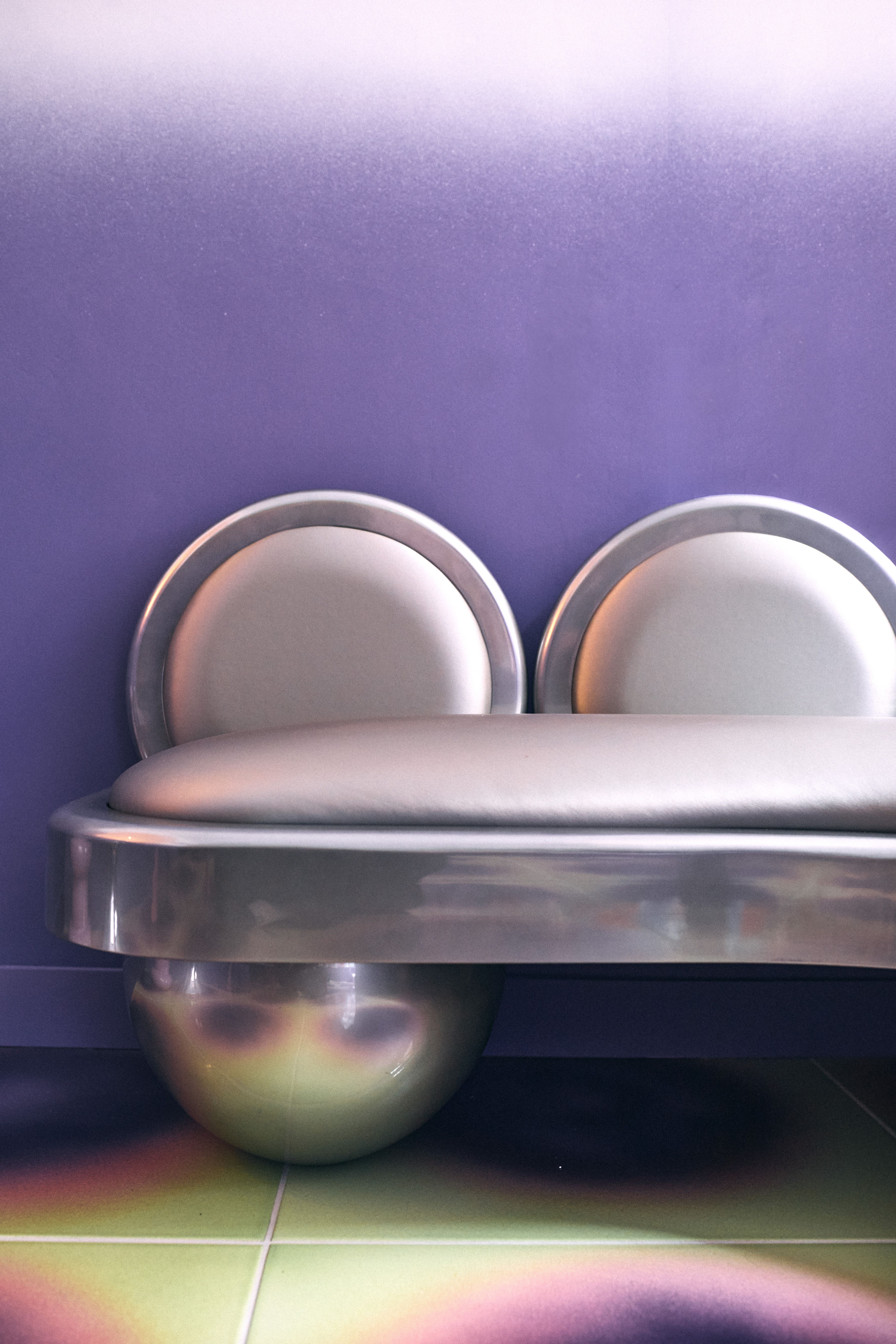 A concept store inspired by a 1960s, futuristic aesthetic features gradient tiles varying from electric green to pink and purple, chrome furnishings, and gradient purple walls leaning o lilac.