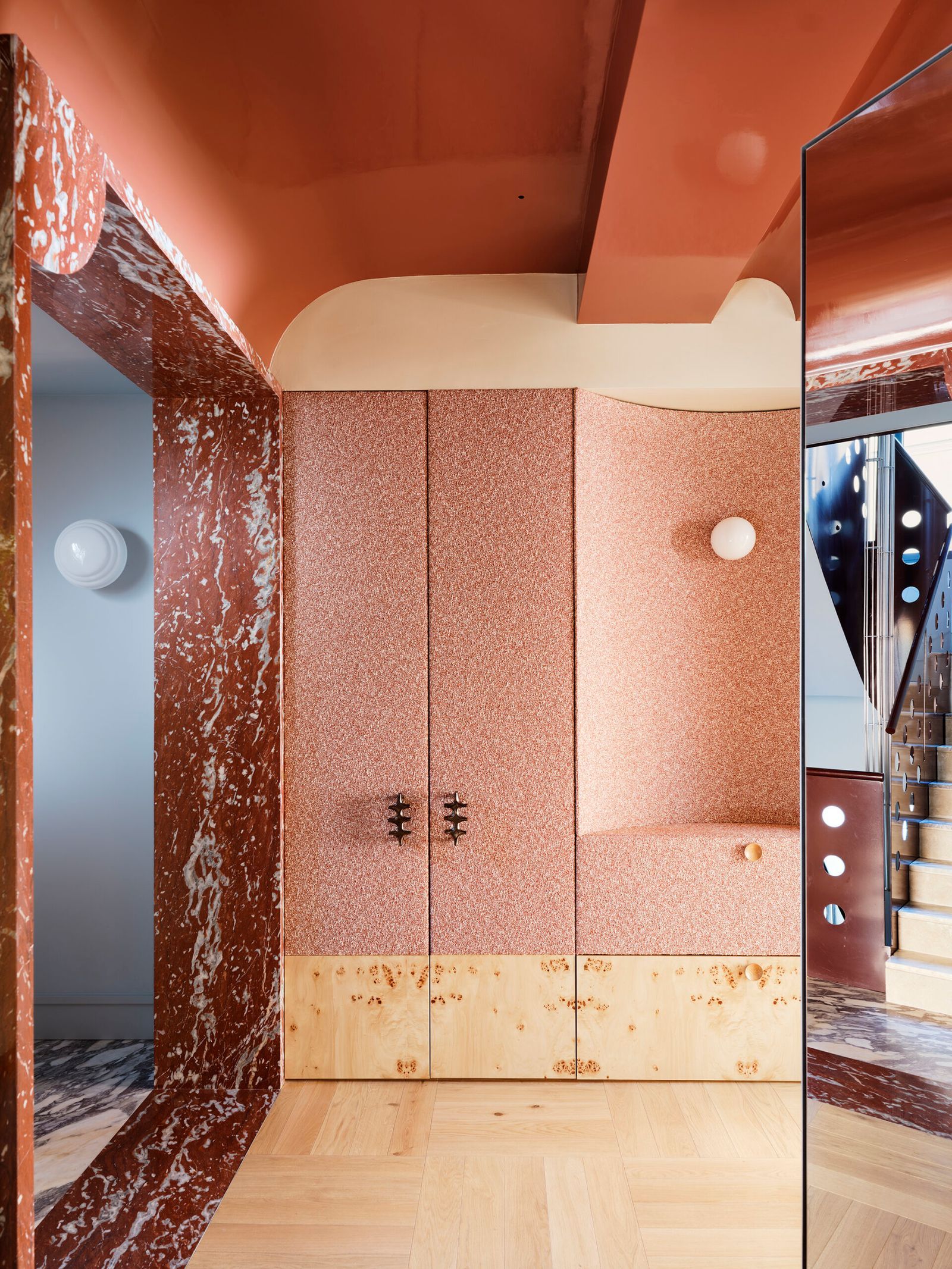 A dressing room with terracotta marble, orange upholstered doors, and a gloss ceiling in complementary tones