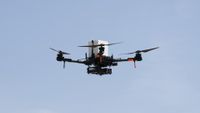 a large quadcopter drone flies in front of a clear, blue sky