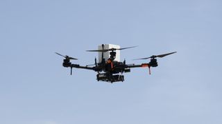 a large quadcopter drone flies in front of a clear, blue sky