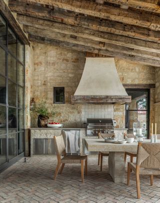 covered outdoor kitchen and dining with exposed wooden rafters and stone walls