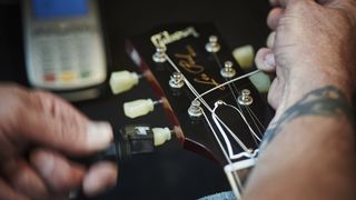 Man uses a string winder to fit a new string to his electric guitar