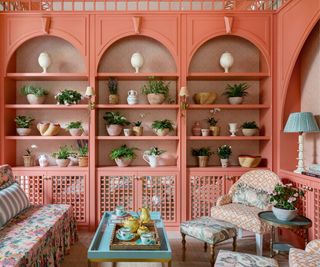 Coral painted tea room with shelves covered in plants and upholstered furniture