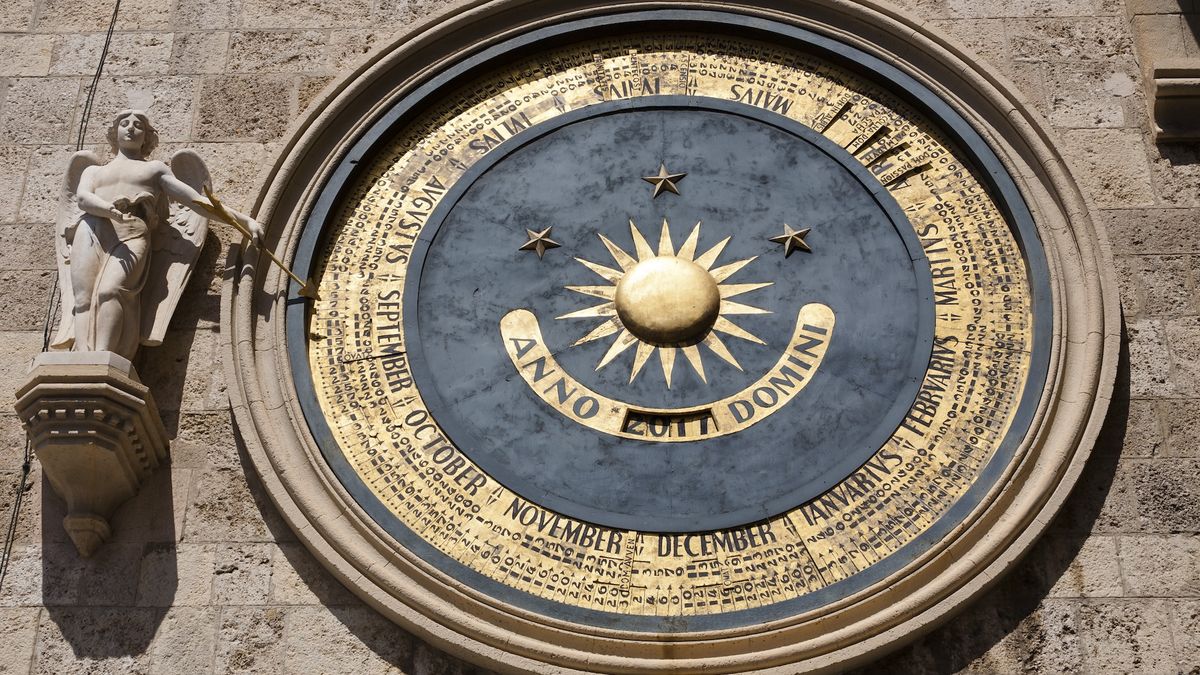 A close-up of a gilded astronomical clock on a clock tower that reads &quot;Anno Domini&quot; in the center