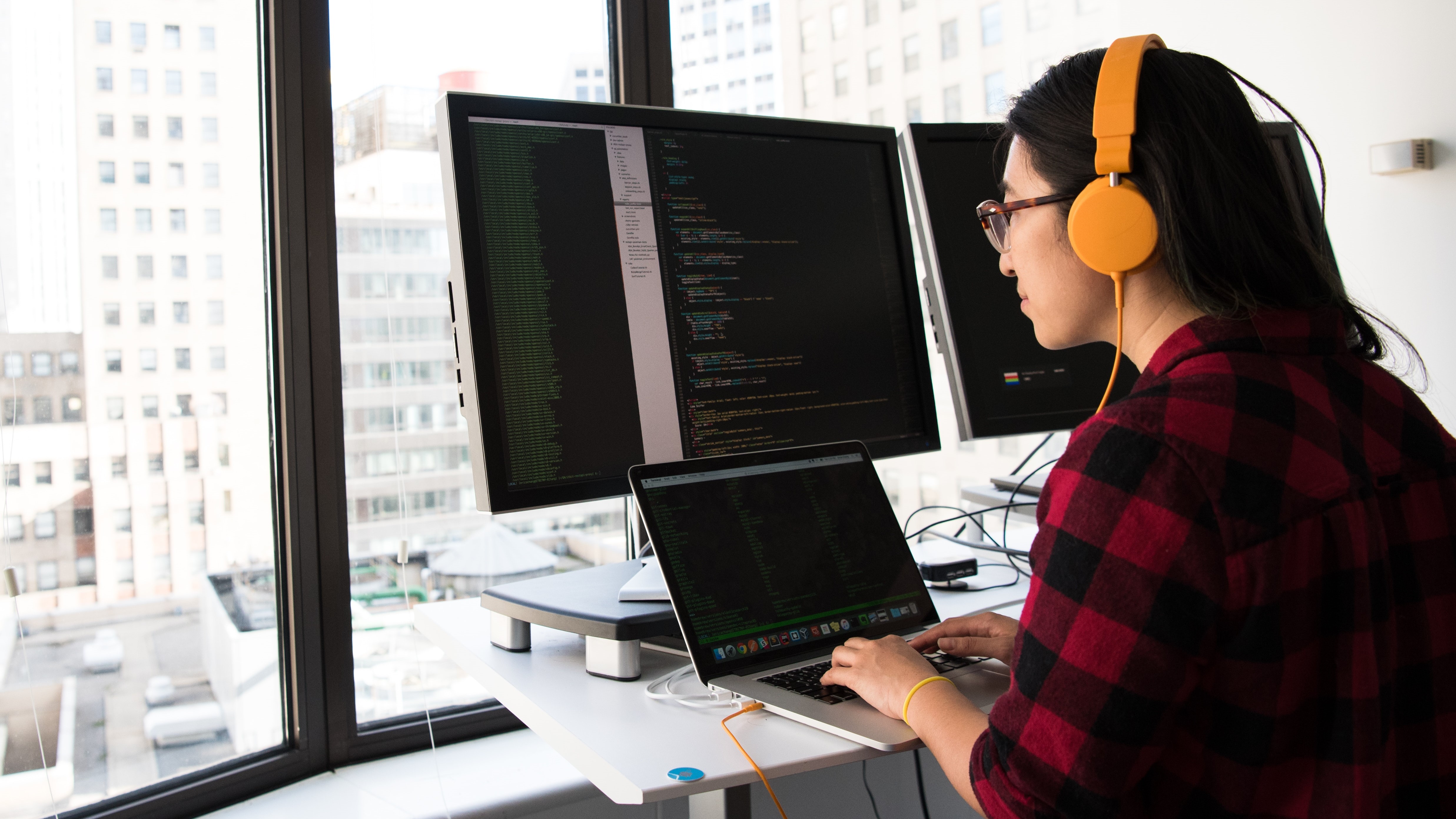 woman coding on multiple computer screens in a high rise office