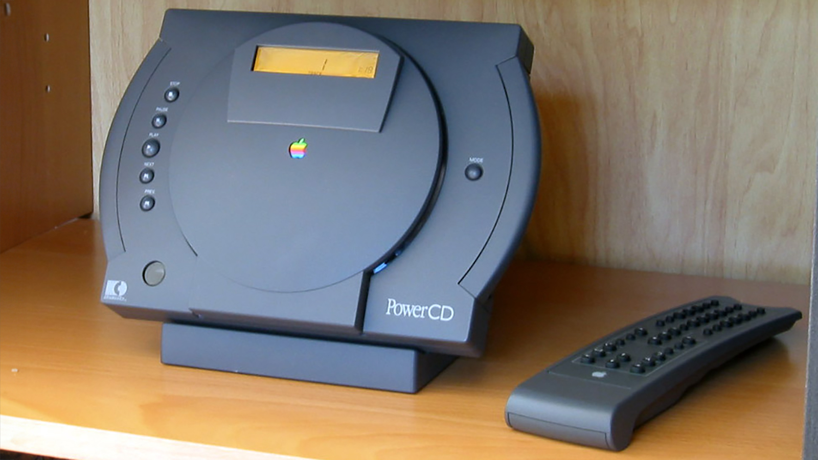 An Apple PowerCD sitting on a shelf next to a remote control