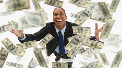 Smiling businessman standing with his arms outstretched and looking upward at falling 100 dollar bills