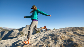 A woman running down a rocky hill with Half Dome in the distance