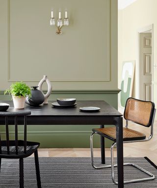 sage green dining room with black table and rattan chair
