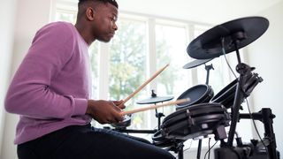 Man in purple jumper plays an electronic drum set