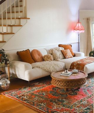 A white couch with a patterned red rug and wooden coffee table