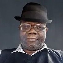 A middle aged man wears frameless glasses and black porkpie hat.