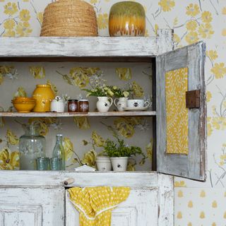 Grey cabinet with shelves in front of yellow patterned wallpaper