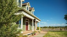 A green painted suburban American home with a lawned front yard, and a view of fields and trees.