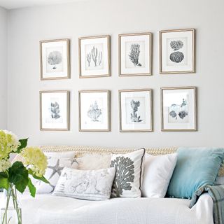 White and grey guest bedroom with eight prints above bed