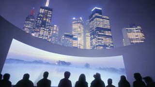 A city skyline with a projection screen below it and people marveling at it. 