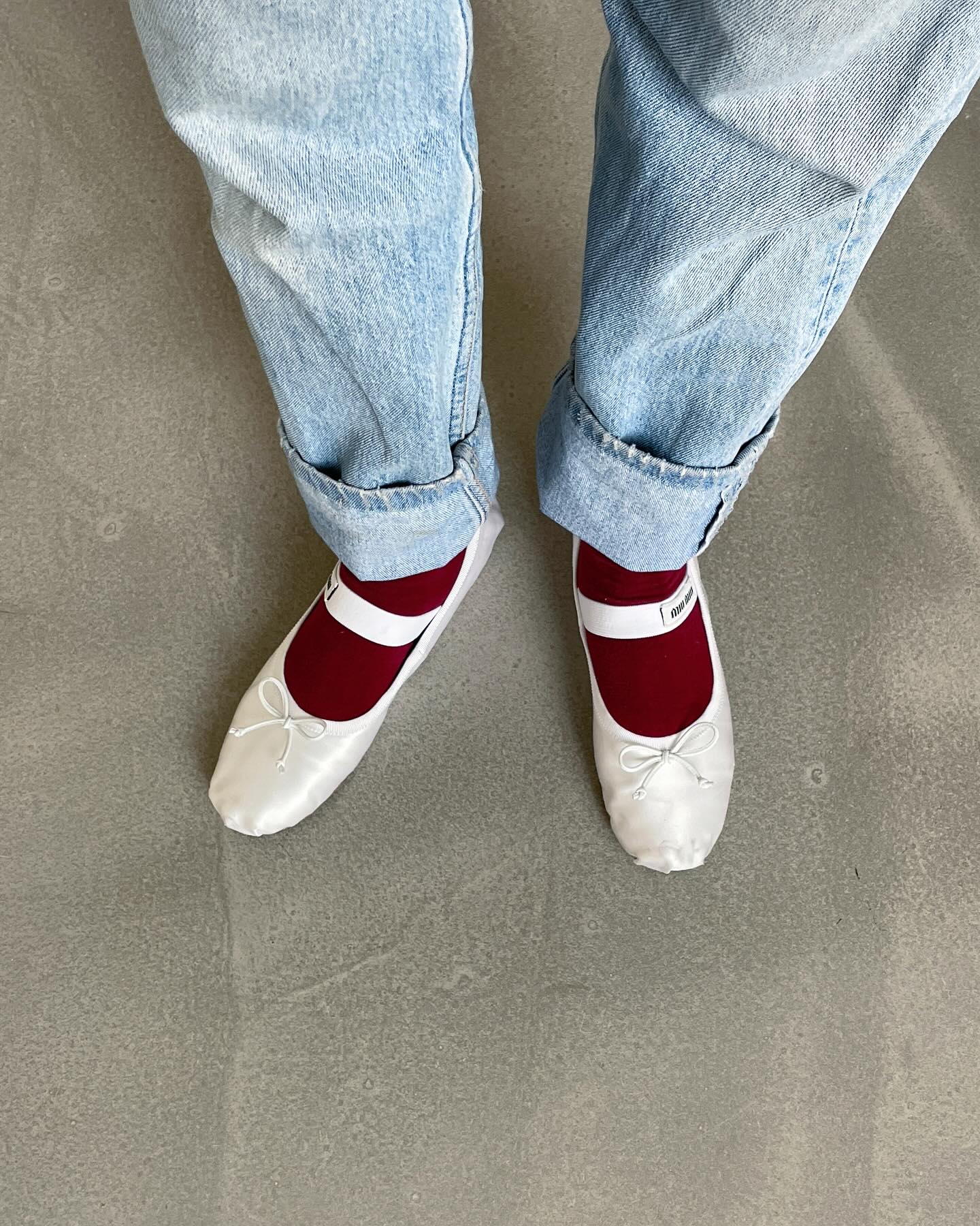 French influencer Anne-Laure Mais wears light-wash cuffed jeans, burgundy red socks, and white Miu Miu ballet flats