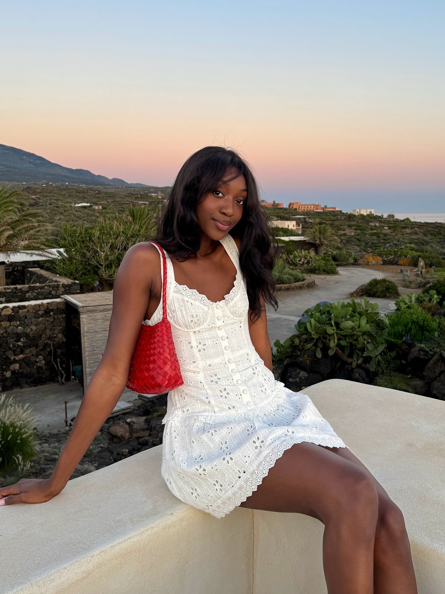 Influencer @emmanuellek_ wears a white mini broderie dress with a red woven shoulder bag.