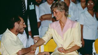 Princess Diana shaking the hand of a AIDS patient in Brazil, she's wearing a pink and yellow blazer and her is in a linen yellow top