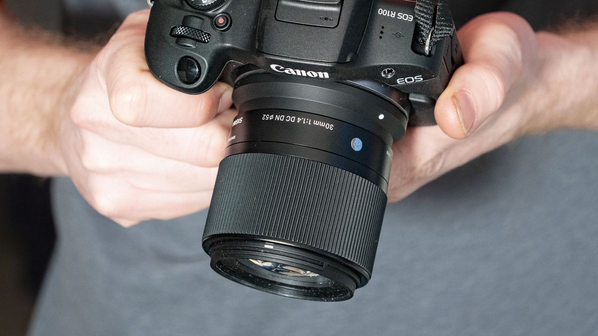 Sigma 30mm F1.4 DC DN Contemporary lens in the hand attached to a Canon EOS R100
