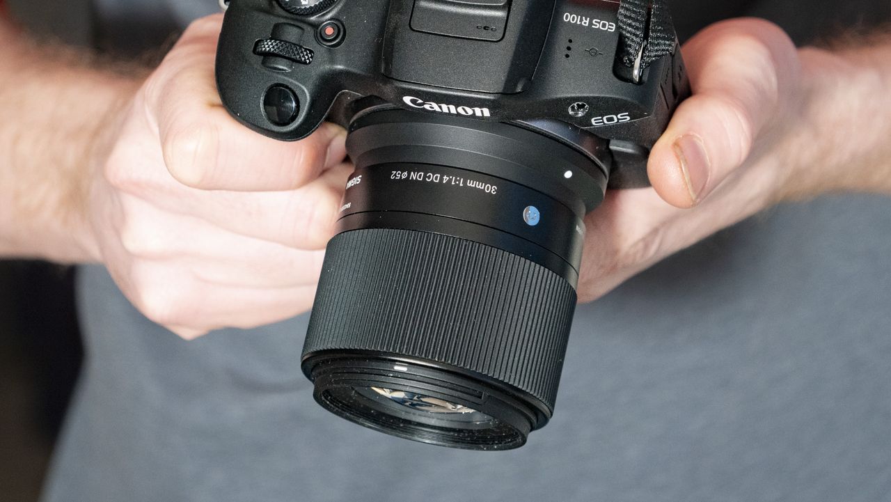Sigma 30mm F1.4 DC DN Contemporary lens in the hand attached to a Canon EOS R100