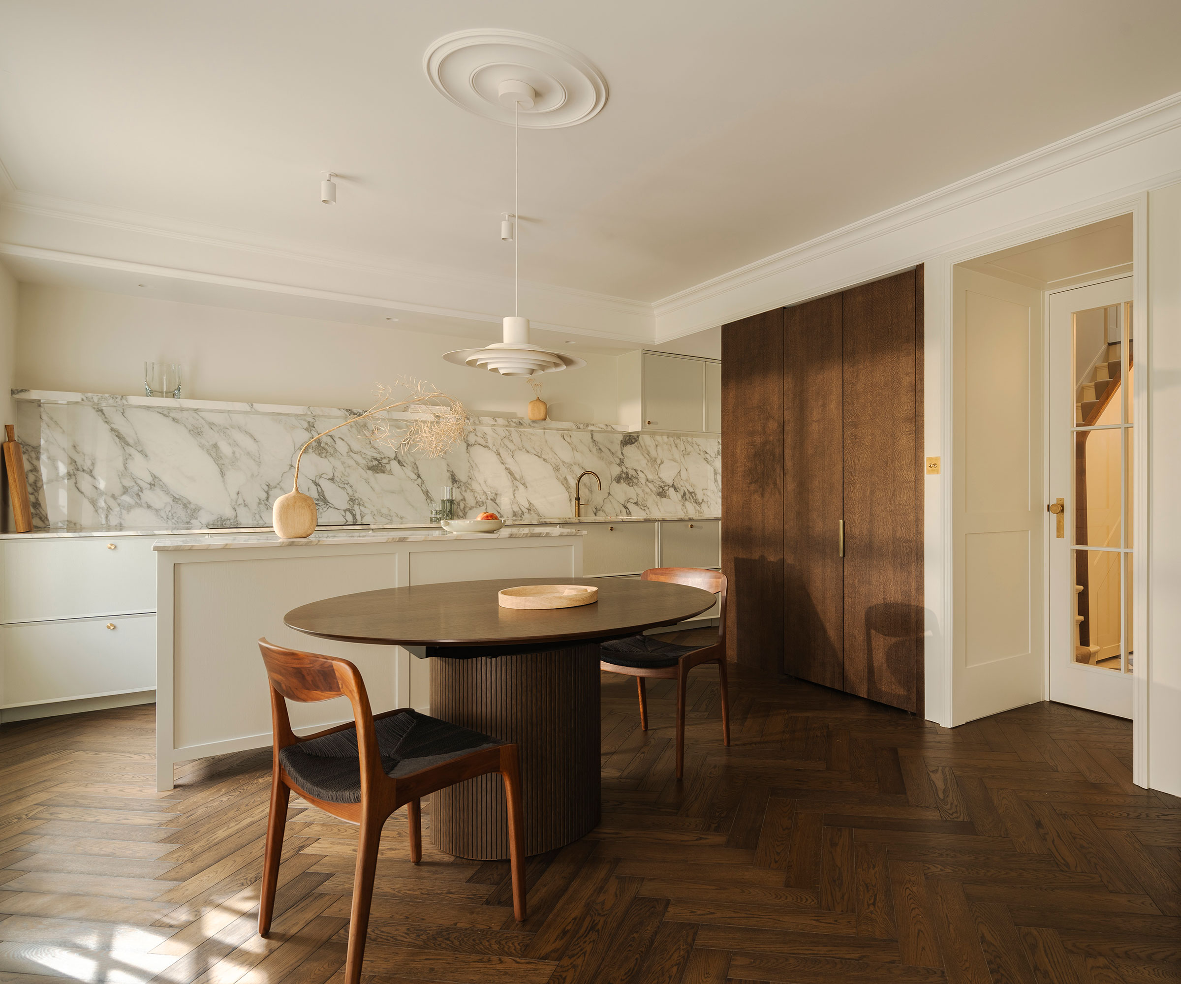 white kitchen with marble splashback and rich wooden herringbone flooring