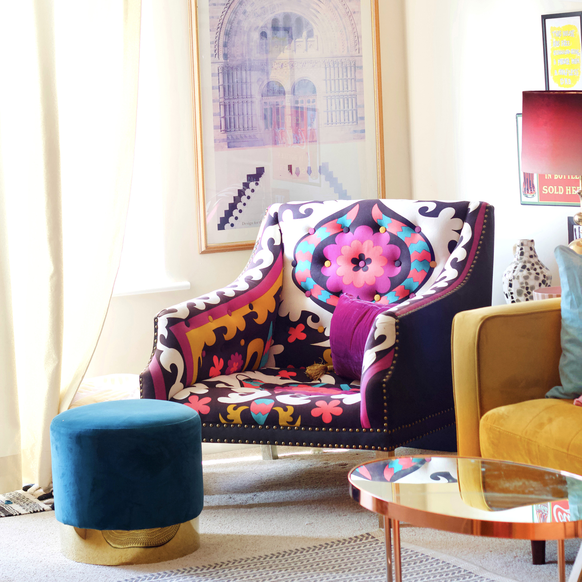 Brightly coloured patterned armchair in a soft yellow living room with a teal velvet footstool in front of it