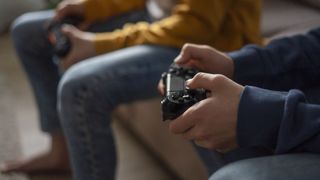 Two people sitting next to each other on a sofa, playing video games using Xbox controllers