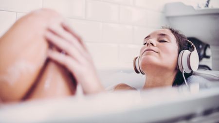 A woman takes a bath while listening to music on headphones