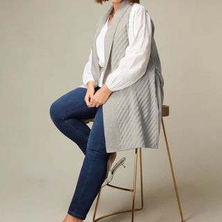 grey sleeveless cardigan worn over a white shirt and jeans