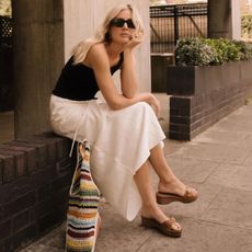 @lucywilliams02 wears a black tank top, white skirt, tan wedges, black sunglasses and a multi-coloured raffia tote bag