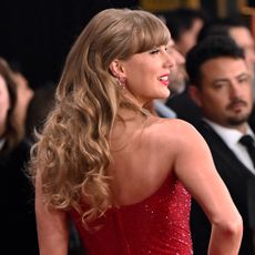 Taylor Swift posing with her back to the camera on the Grammys red carpet in a glittering red dress and curly hairstyle 