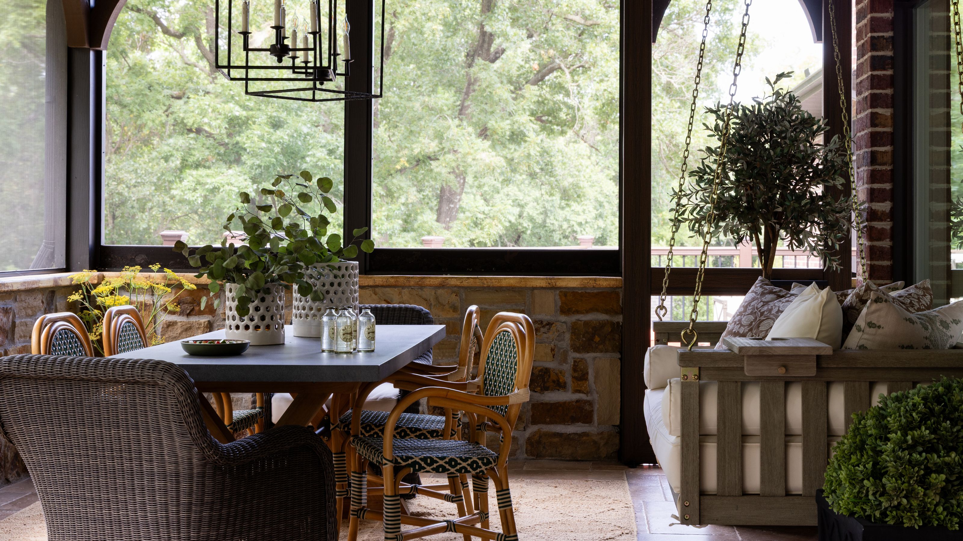 a covered porch overlooking the surrounding woods with a porch swing and bistro dining area