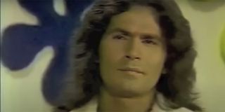 Rodney Alcala with long hair sitting on a chair playing The Dating Game.